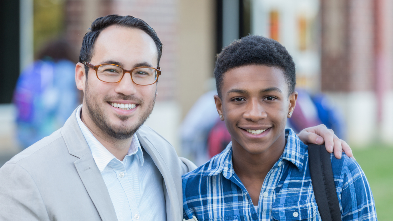 Two individuals standing together in front of a school