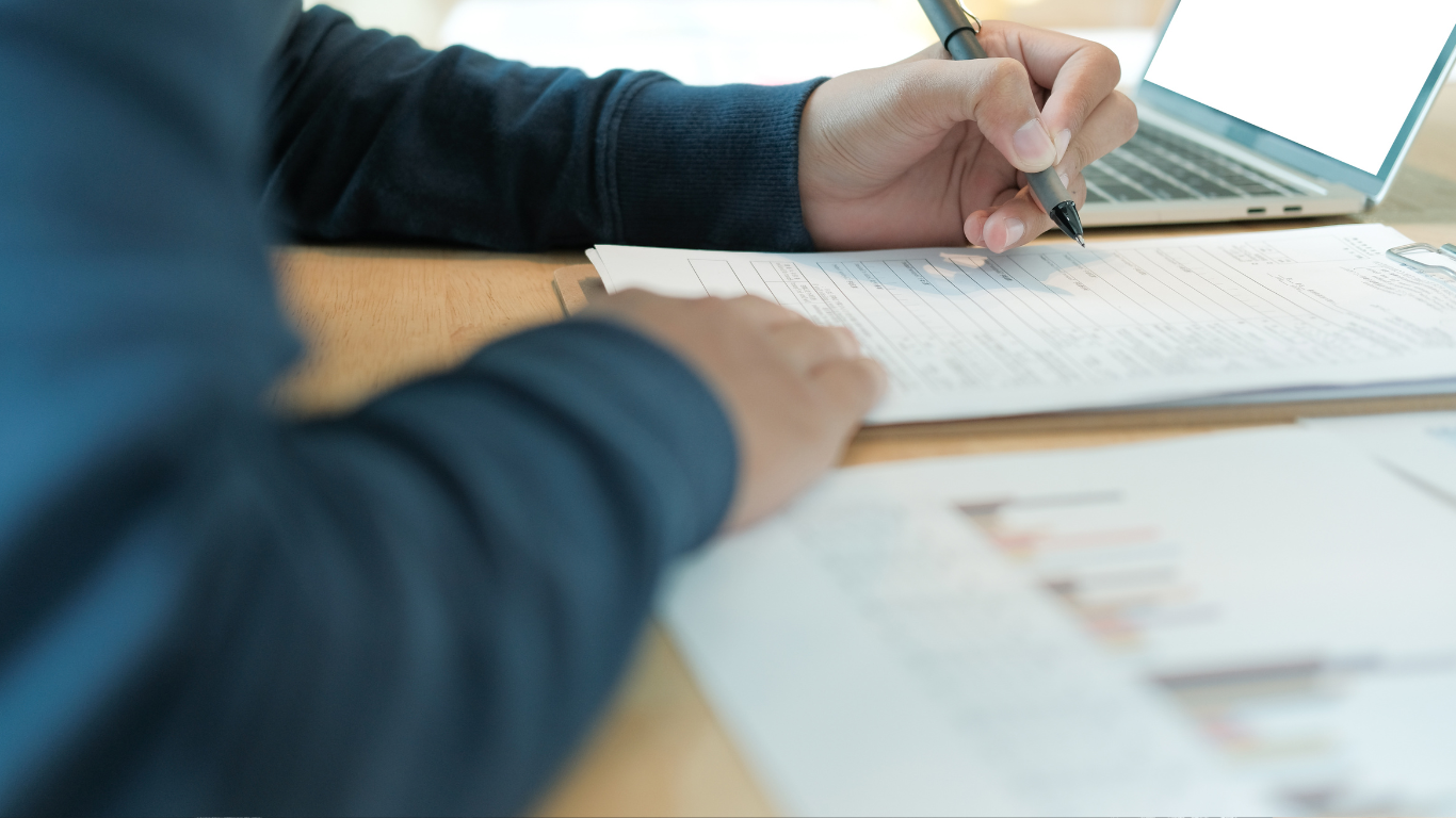 a person sitting at a table with a laptop and pen